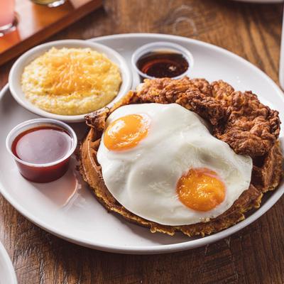 Chicken and waffles accompanied by two fried eggs, cheese grits, and dipping sauces
