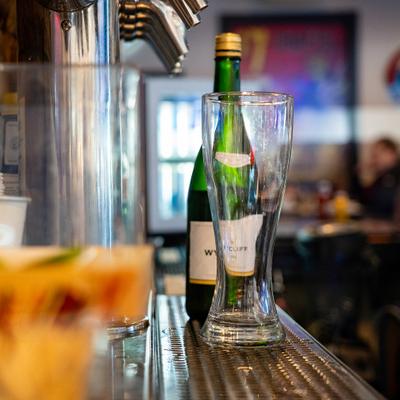 Pilsner glass sitting on a metal bar top with a bottle, near a draft beer tap system.