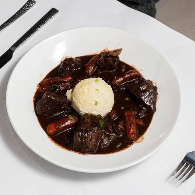 Chunks of beef simmered in a rich red wine gravy, with sausage and mashed potato.
