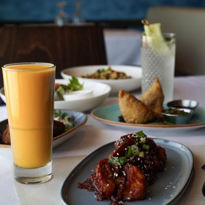 A spread of dishes on a table including samosas, Indian appetizers, and mango lassi.