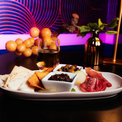 Charcuterie plate with cured meats, cheeses, olives, jam, and crackers.