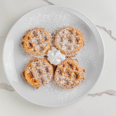 Mini waffles dusted with powdered sugar and served with whipped cream.