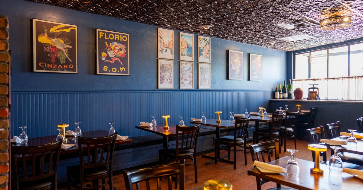 A cozy restaurant with blue walls, vintage posters and tables set with glasses and napkins