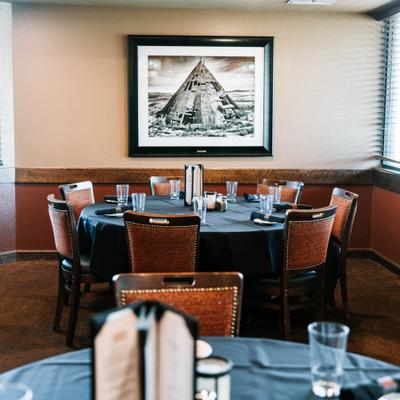 Dining room with round tables covered in dark tablecloths, surrounded by upholstered chairs.
