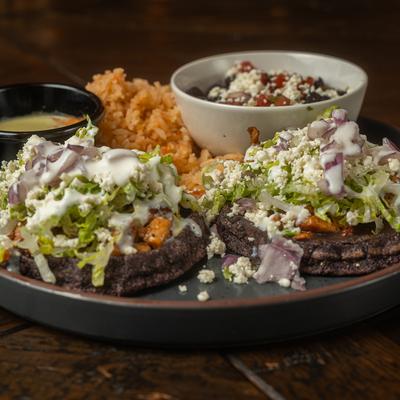Plate with two tacos topped with lettuce, cheese, and onion, served with rice, beans, and sauce.