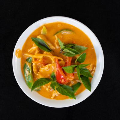 Red curry with vegetables in creamy orange sauce, topped with fresh basil leaves.