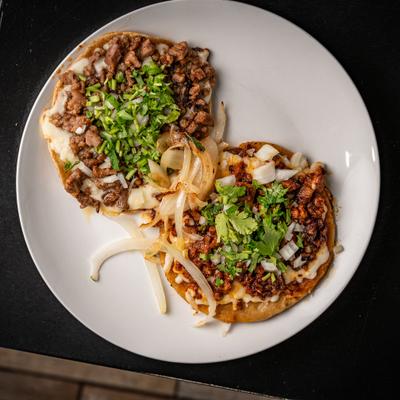 Tostada and taco topped with melted cheese, meat, onions, and cilantro.