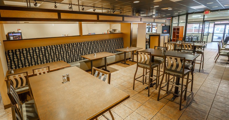 Interior of a restaurant with wooden tables, patterned seating, and natural light from glass doors