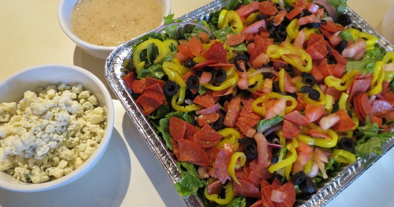 Chopped salad with pepperoni, olives, and banana peppers, served with dressing and cheese