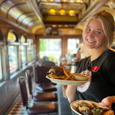 A friendly waitperson holding plates of food in the diner setting.
