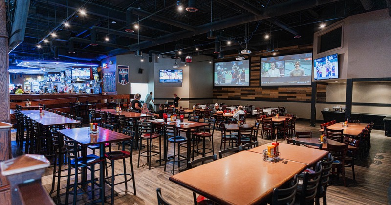 Interior, seating area, various table setups, bar in the back, TVs, projector sreens