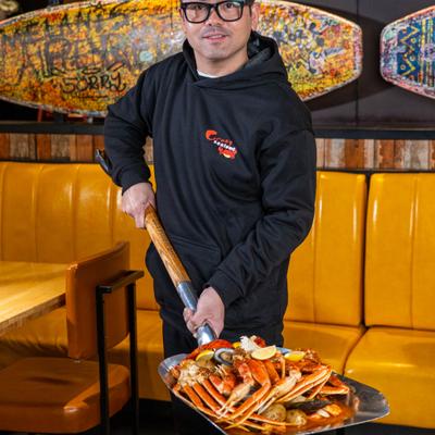 A server holding a large shovel of seafood boil in dining area.