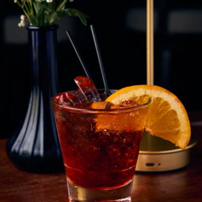 Red cocktail garnished with an orange slice on a wooden table.