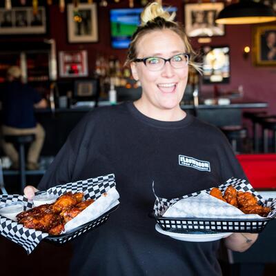 Smiling Staff member serving baskets of chicken wings