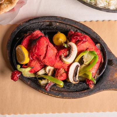 A cast iron skillet with tandoori chicken served with peppers and mushrooms.