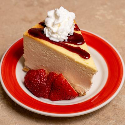 Cheesecake with fresh strawberries, strawberry sauce drizzle, and whipped cream.