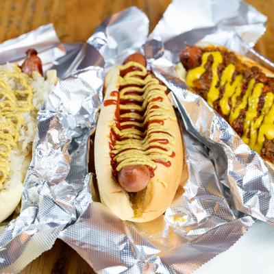 Assorted hot dogs drizzled with mustard served on foil paper.