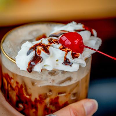 Espresso Martini with whipped cream, chocolate sauce drizzle, and a cherry on top.