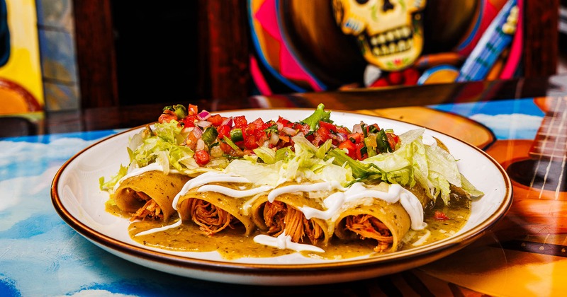 Enchiladas, topped with salsa, lettuce, and sour cream