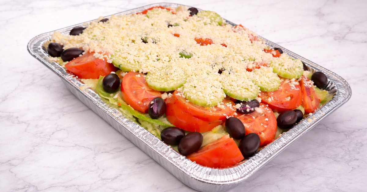 Greek salad topped with a layer of crumbled feta cheese, served in a catering tray