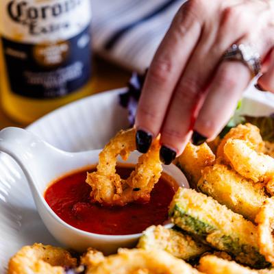 A person dips a calamari bite into marinara sauce, close up.