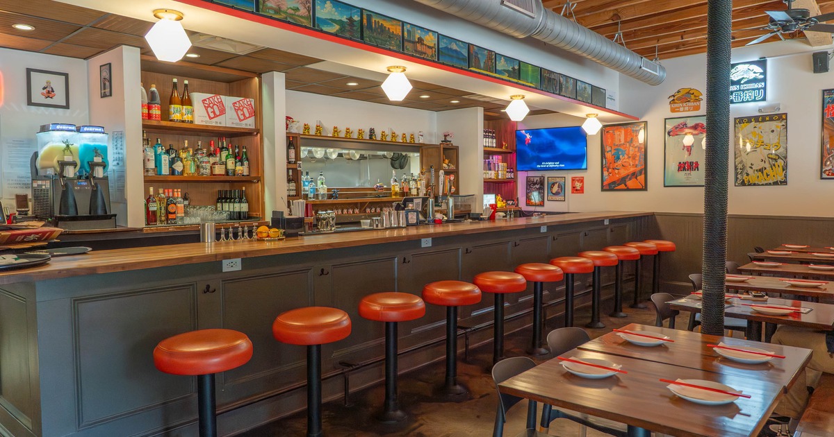 Interior of a bar with red stools and wooden tables, decorated with colorful posters
