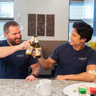 Two guests smiling and clinking beer bottles at a bar counter.