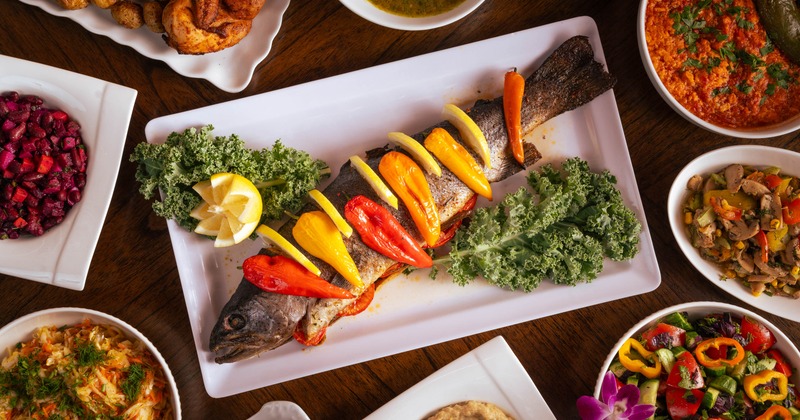 Whole roasted fish on platter surrounded by colorful side dishes