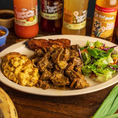 Curry Goat served with sides of jalapeno mac and cheese, toss salad, and plantains.