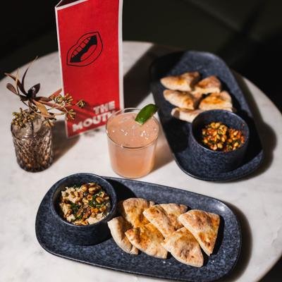A cocktail and small plates, with pita bread and salads set on a table.