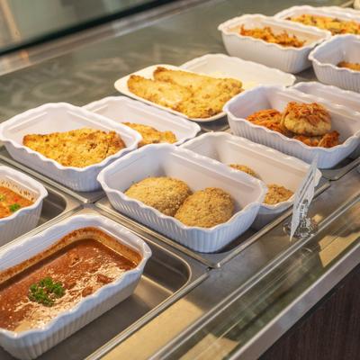 Service counter displaying a variety of pre-prepared dishes in white containers.