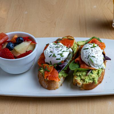 Avocado toast topped with salmon and sour creme, alomgside a bowl of friuts.