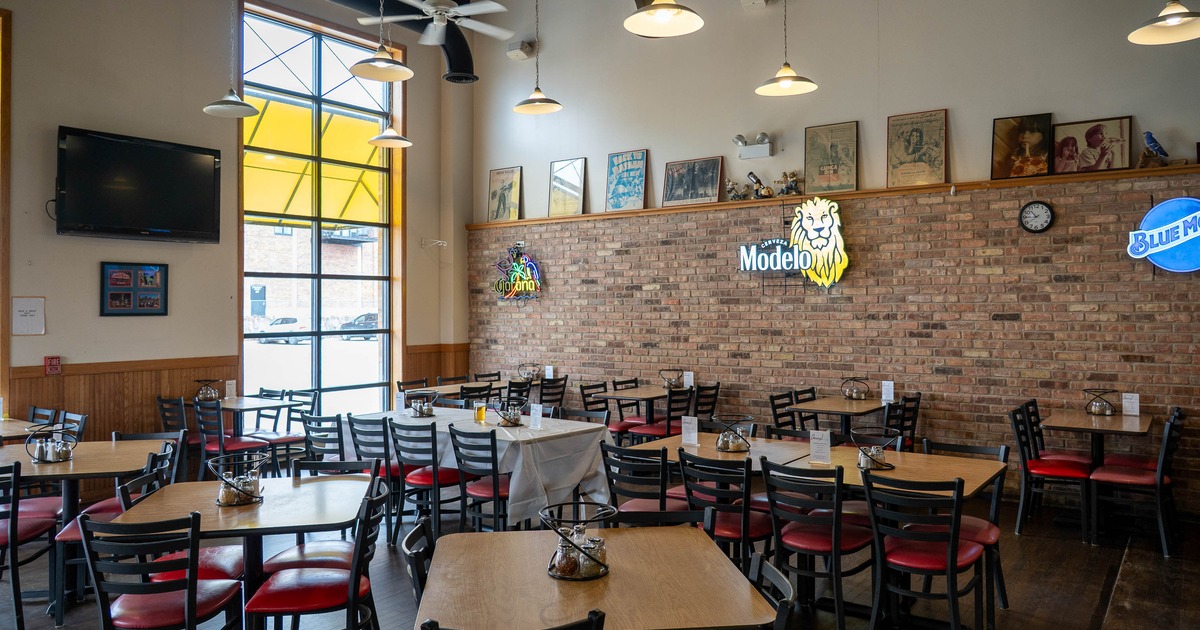 Restaurant interior with tables, chairs, brick wall and neon signs.