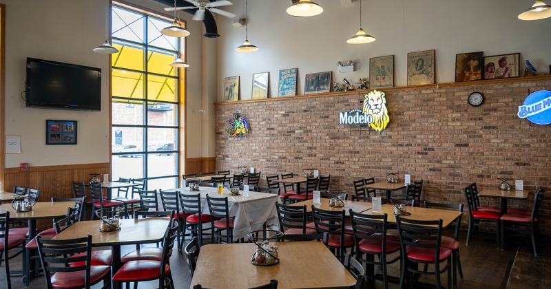 Restaurant interior with tables, chairs, brick wall and neon signs.