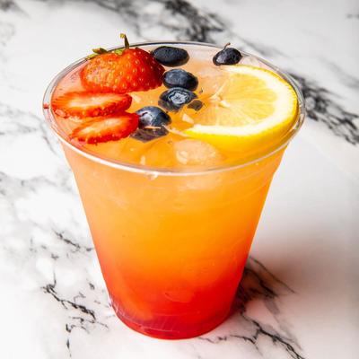 A layered cocktail with strawberries, blueberries, and a lemon slice.