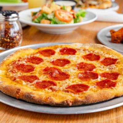 Pepperoni pizza on a round metal tray, accompanied with other food plates.