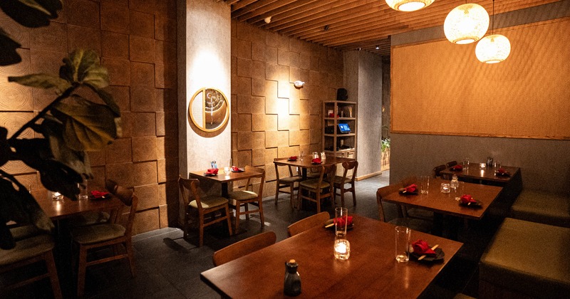 A warmly lit interior with wooden decor, pendant lights and neatly set tables
