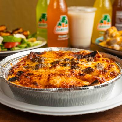 Enchiladas covered in melted cheese, with various food and drinks in the background.