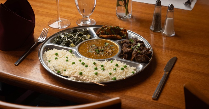 Indian thali with rice, lentils, greens, and meat dishes on a metal platter