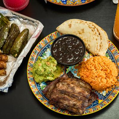 Grilled meat, black beans, rice, guacamole, and warm tortillas on a plate.