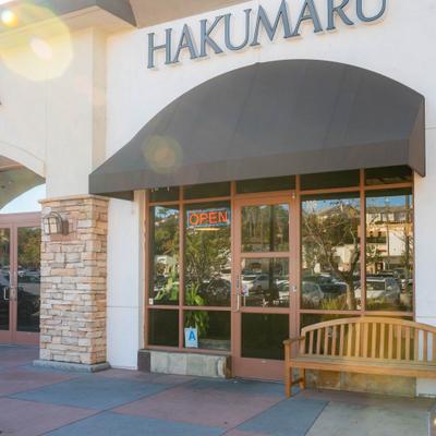 Hakumaru restaurant exterior with an Open sign and a wooden bench.