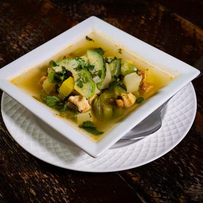 Chicken soup in a white bowl served on a white plate.