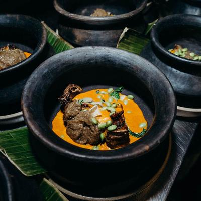 Black clay bowls filled with vibrant orange sauce, tender meat, and herbs.