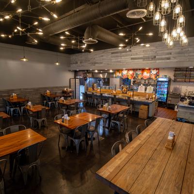 Interior with table seating, dark ceilings, wood-panelled accents and hanging light fixtures.