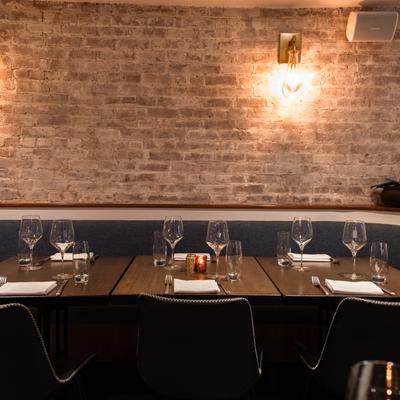 Interior, banquette by a rustic brick wall, with set tables and chairs