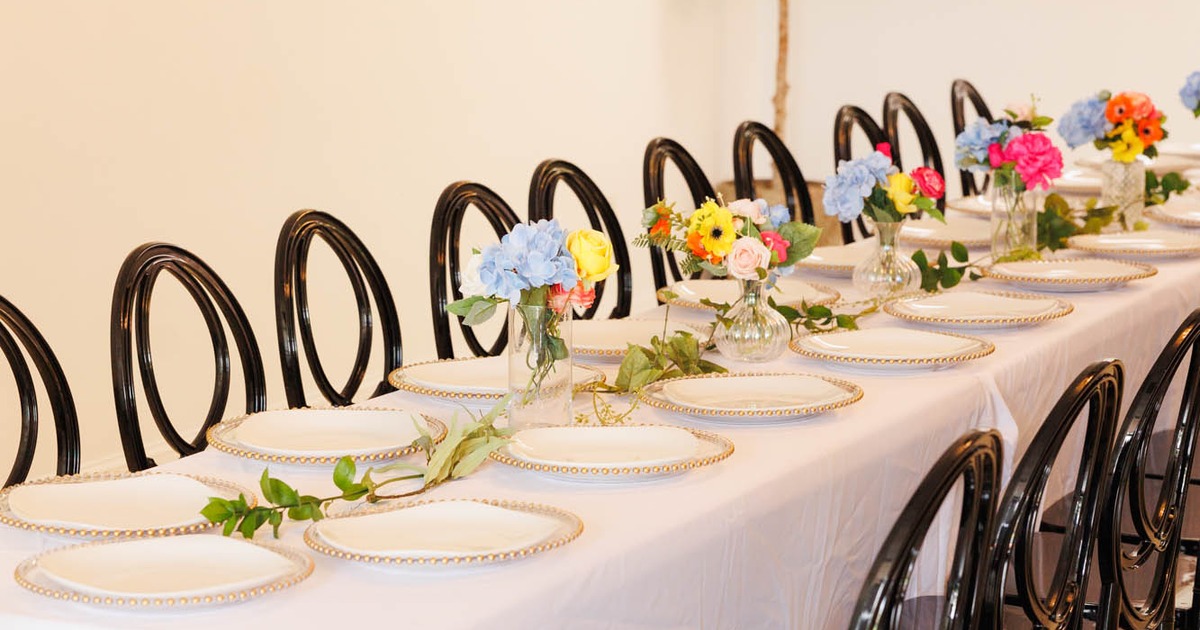 A long dining table with white cloth, gold-edged plates, and black chairs