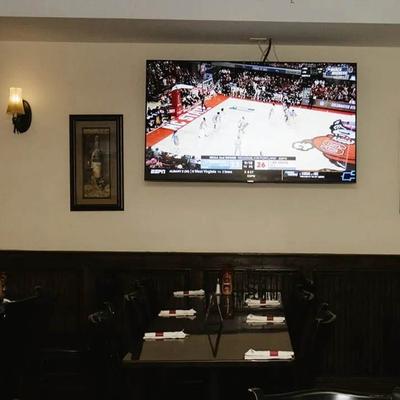 Dining area with set tables and a large TV showing a basketball game.