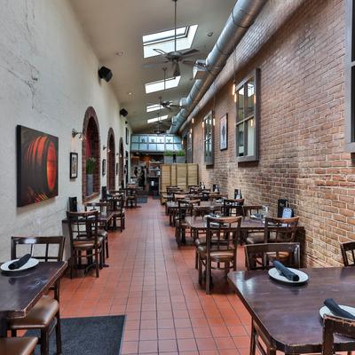 Restaurant interior with brick walls and skylights, wooden tables with plates and black napkin.
