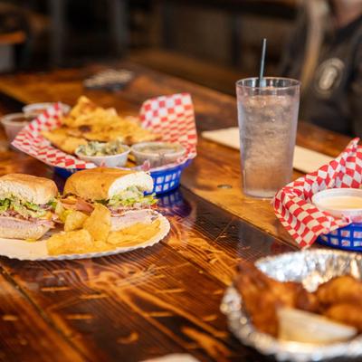 A spread of food, including sandwich, fries, pretzels, and wings on a rustic wooden table.