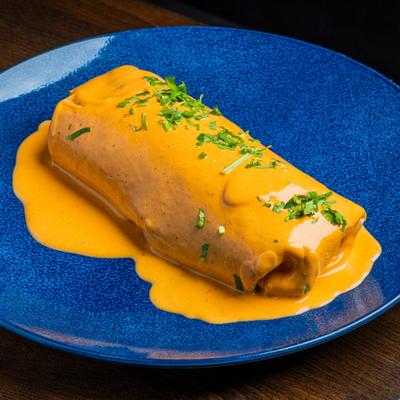 Burrito smothered in orange cheese sauce and garnished with chopped herbs.